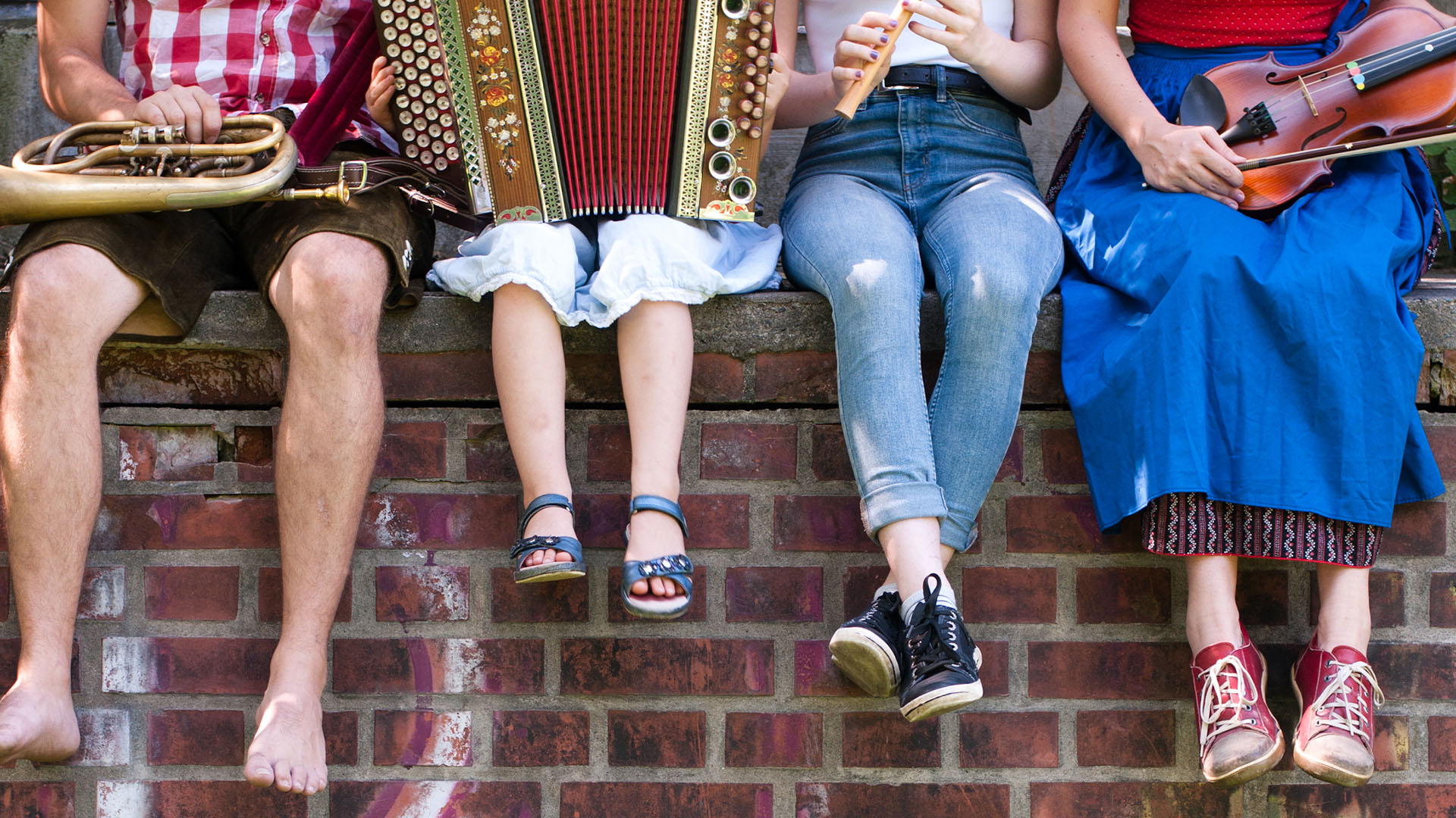 Junge Menschen sitzen auf einer Mauer und musizieren.